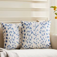 two blue and white pillows sitting on top of a couch next to a vase with flowers