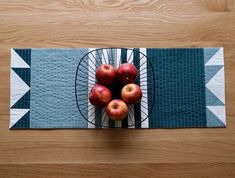 four apples in a basket on top of a placemat with an arrow pattern and blue background