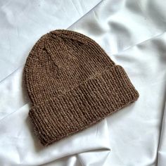 a brown knitted hat laying on top of a white bed sheet covered in sheets