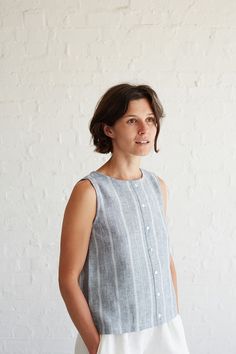 a woman standing in front of a white wall wearing a gray and white striped top