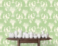 several white vases on a wooden table in front of a wallpapered background