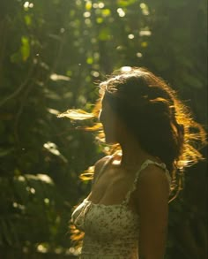 a woman standing in front of trees with her hair blowing in the wind and sunlight shining through