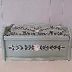 a green box with flowers painted on the side and leaves in the middle, sitting on a table