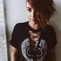 a woman with tattoos on her arms and chest standing next to a wall wearing a black t - shirt