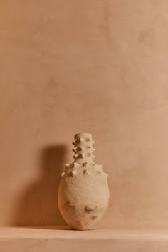 a white vase sitting on top of a shelf in front of a wall with a brown background