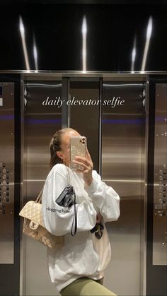 a woman taking a selfie with her cell phone in front of a stainless steel elevator