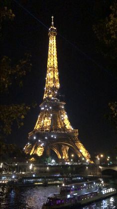 the eiffel tower lit up at night with boats passing by on the water