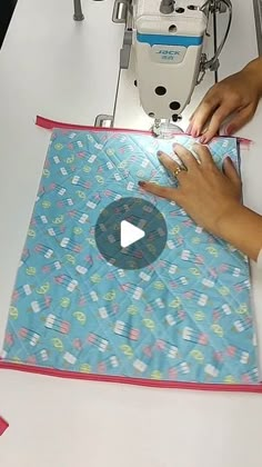 a woman is working on a piece of fabric with scissors and sewing machine in the background