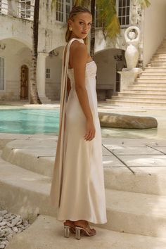 a woman standing in front of a pool wearing a white dress and long scarf over her shoulders