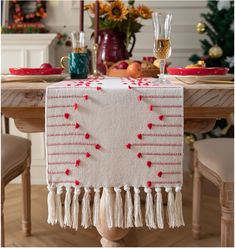 a table topped with a white and red table cloth covered in tassels on top of a wooden table