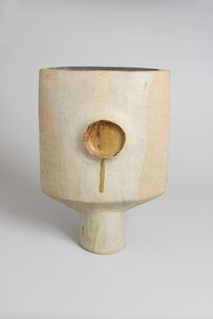 a white vase with a wooden spoon sticking out of it's side, on a gray background