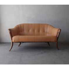 a brown leather couch sitting on top of a cement floor next to a wall and window