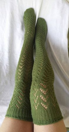 the legs of a woman wearing green knitted socks with holes in them, laying on a bed