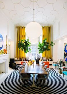 a dining room table surrounded by chairs in front of a fire place and yellow curtains