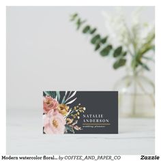 a business card with flowers on it next to a vase and greenery in the background