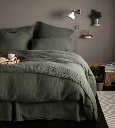 a bed with green linens and pillows in a dark room next to a lamp