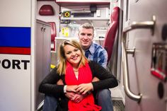 a man and woman are sitting on the door of a fire truck, smiling at the camera