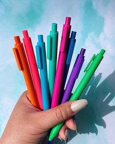 a woman's hand holding several different colored pens in their palm, with the top one painted white