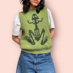 a woman wearing a green knitted sweater with a frog design on it's back