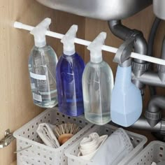 three bottles of soap and other cleaning products in a kitchen sink under a faucet