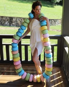 a woman in a white dress is holding a large stack of doughnuts while standing on a porch