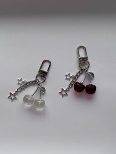 two charms with cherries attached to them on a white surface, one is red and the other is silver