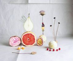 various fruits and vegetables are arranged on a white table top, with one cut in half