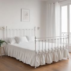 a white bed sitting in the middle of a bedroom next to a window with curtains