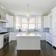 a large kitchen with white cabinets and wood flooring, along with an island in the middle