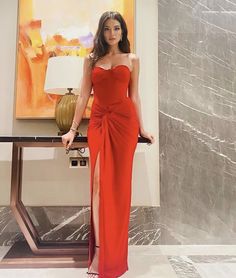 a woman in a red dress standing next to a table with a painting on it