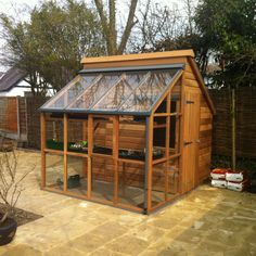 a small wooden greenhouse in the middle of a backyard with an enclosed patio area and potted plants