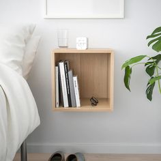 a book shelf with books and slippers on the floor in front of a bed