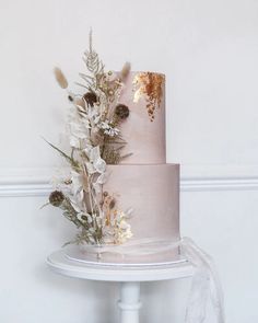 a three tiered cake with white flowers and greenery on the top is sitting on a table