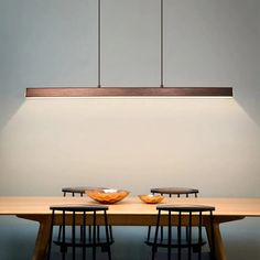 a wooden table with two bowls on it and three lights hanging from the ceiling above