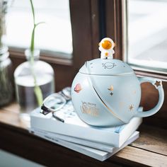 a blue teapot with an animal on it sitting on top of a stack of books