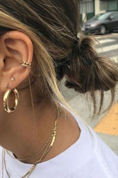 a woman wearing gold earrings and a white t - shirt is standing on the street