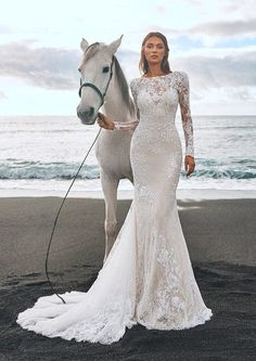 a woman standing next to a white horse on top of a sandy beach near the ocean