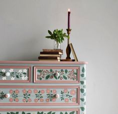 a pink dresser with flowers painted on it and a candle in the corner next to it