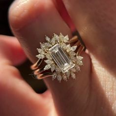 a close up of a person's hand holding a ring with an emerald stone