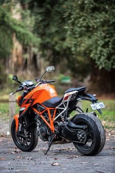 an orange and black motorcycle parked on the side of a road in front of trees