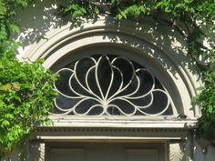 the front door to an old building with a decorative window above it and green leaves on the outside