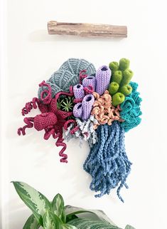 a bunch of crocheted flowers are hanging on the wall next to a plant