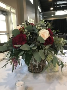 a centerpiece with flowers and greenery on a white table cloth at a wedding reception