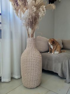 a cat sitting on the floor next to a vase with dry grass in it