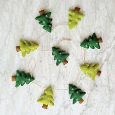 small felt christmas trees are arranged on a marble surface, with twine and thread