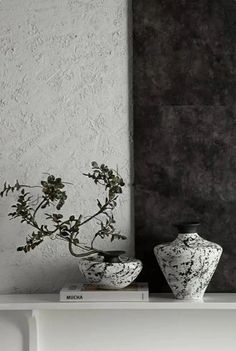 two vases sitting on top of a white shelf next to a black and white painting