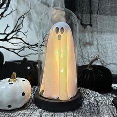 a lighted ghost in a glass dome next to two pumpkins on a table with black and white decorations