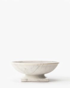 a white marble bowl sitting on top of a wooden stand in front of a white wall