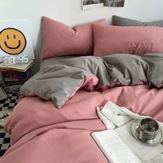 a bed with pink and grey sheets, pillows and an open book on top of it