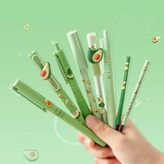 a hand is holding seven green pens with cartoon characters on them and an avocado in the middle